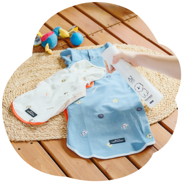 カーペットに並べたペット用衣服にマイクロミストスプレーを吹きかけている写真